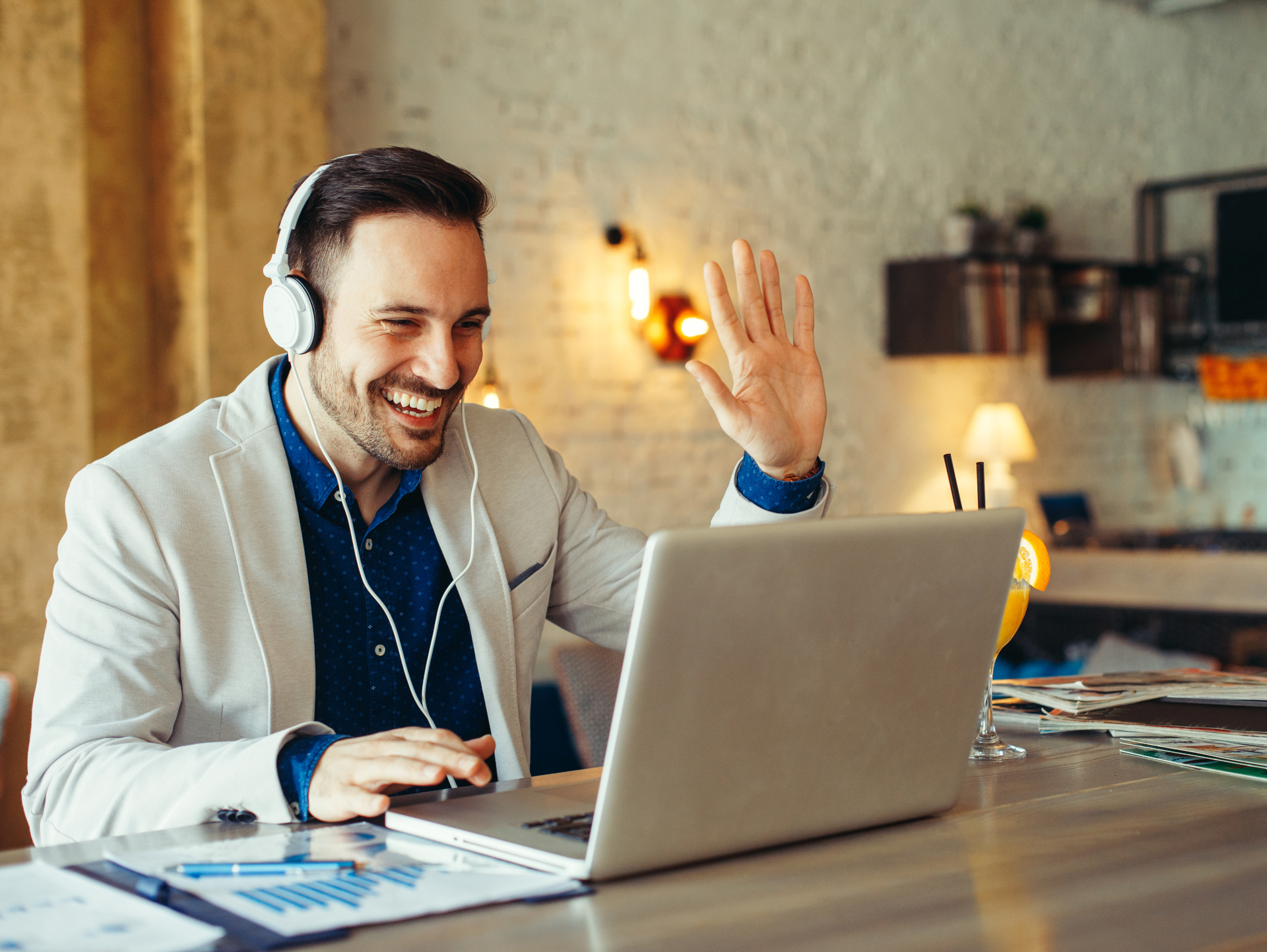 Mann mit Headset vor Notebook, der in die Kamera winkt