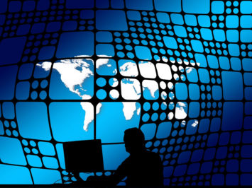 Person an PC als Schattenriss vor Weltkugel-Hintergrund