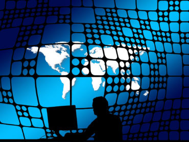 Person an PC als Schattenriss vor Weltkugel-Hintergrund